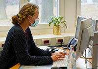 Eine Frau mit Mund-Nasen-Schutz am Computer