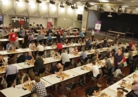 Eine Halle voller schachspielender Menschen an vielen Tischen. 