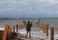 Die Rückansicht eines Mannes, der mit einem Megafon am Strand steht. 