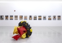 Ein LKW-Reifen liegt vor einer Reihe mit Bildern in einem Ausstellungsraum. 